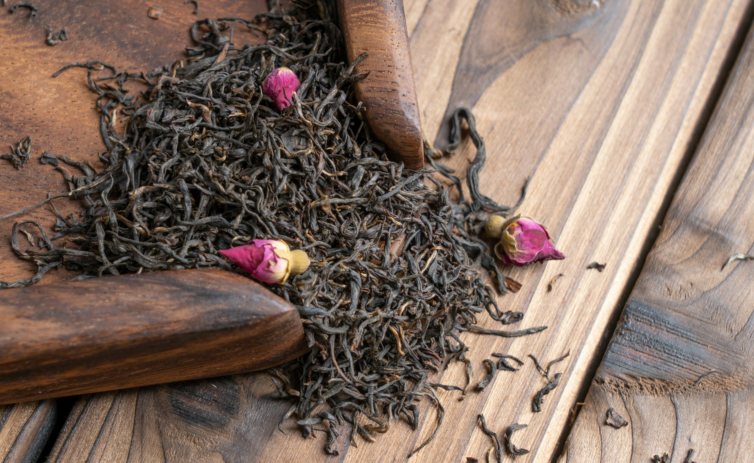 Loose black tea leaves and dried rosebuds on dark wood